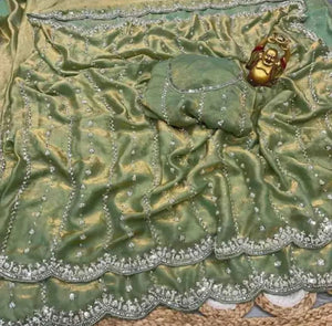 Green fabric with silver embroidery and a gold decorative element on a textured surface.