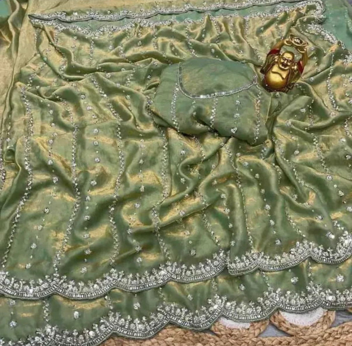 Green fabric with silver embroidery and a gold decorative element on a textured surface.