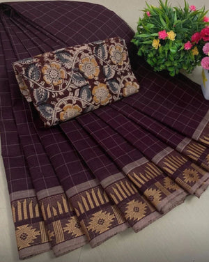 Brown saree with floral patterns on a bed, accompanied by a decorative pillow and flowers.